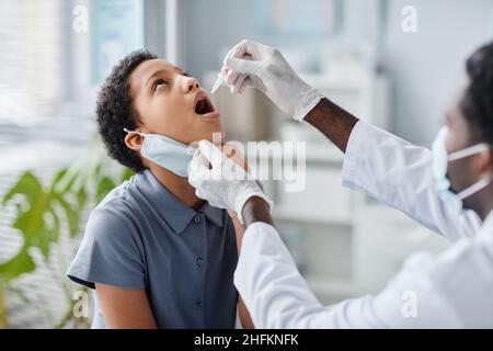 Afro-américain du médecin qui larde du liquide dans la bouche de l'enfant pendant la vaccination orale en clinique Banque D'Images