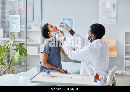 Vue latérale portrait afro-américain d'un médecin qui dépose du liquide dans la bouche de l'enfant pendant la vaccination orale en clinique Banque D'Images