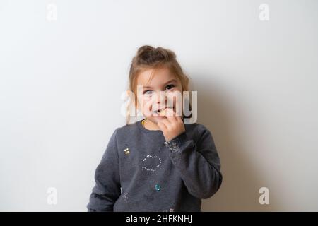 Portrait en gros plan de Nice mignon adorable jolie petite fille gaie mordant de la nourriture et posant à l'appareil photo isolé sur fond blanc Banque D'Images