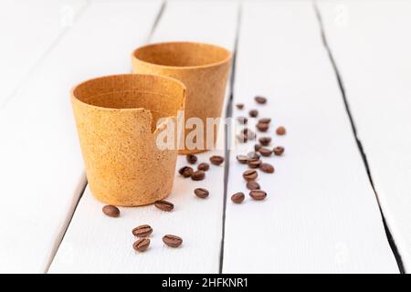 Tasses à café gaufré écologiques avec grains de café rôtis sur une table en bois blanc Banque D'Images