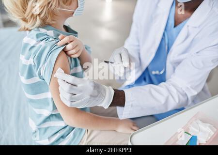 Gros plan d'un médecin méconnaissable qui vaccine un petit garçon mignon dans une clinique de vaccination des enfants, espace copie Banque D'Images