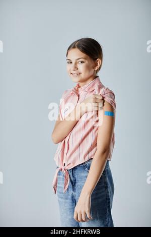 Portrait vertical d'une jeune fille adolescente mignonne montrant une zone d'épaule et souriant à l'appareil photo après avoir été vaccinée Banque D'Images