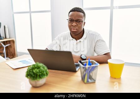 Jeune africain travaillant au bureau en utilisant un ordinateur portable regardant endormi et fatigué, épuisé pour la fatigue et la gueule de bois, les yeux paresseux le matin. Banque D'Images