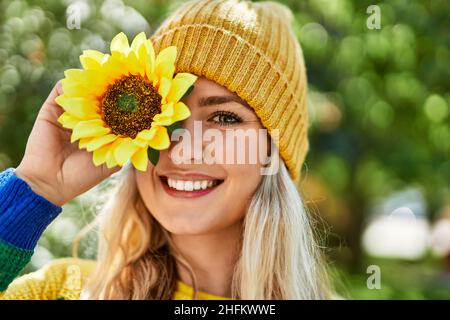 Jeune femme blonde souriant avec du tournesol à l'œil au parc Banque D'Images