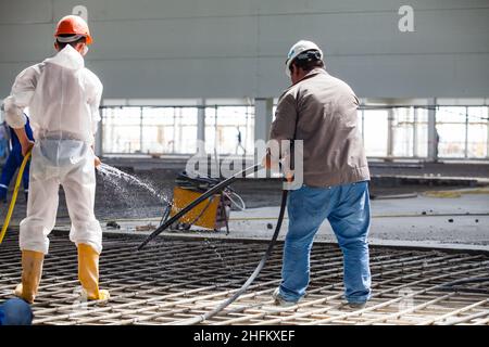 Atyrau, Kazakhstan - mai 21,2012 : nouvelle usine Chevron. Construction d'un nouveau bâtiment industriel. Les ouvriers arrosoir le plancher pour bétons (verser). Banque D'Images