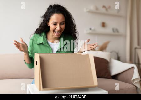 Joyeuse femme Shopaholic criant dans l'excitation ouverture de boîte en carton intérieur Banque D'Images