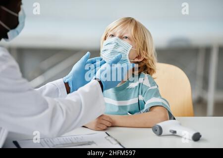 Médecin méconnaissable examinant un petit garçon portant un masque à la clinique de vaccination des enfants, espace de copie Banque D'Images