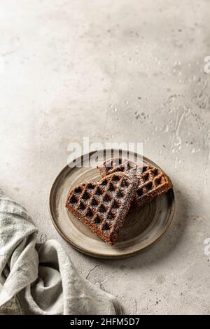 Deux gaufres au chocolat en forme de coeur dans une plaque en céramique sur fond texturé avec une serviette en lin au premier plan, encore la vie pour la Saint-Valentin Banque D'Images