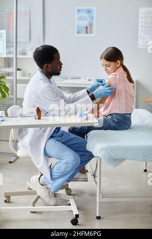 Portrait vertical de la petite fille courageuse se faisant vacciner contre le COVID-19 dans une clinique de vaccination des enfants Banque D'Images