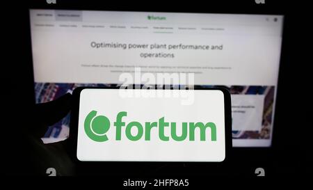 Personne tenant un téléphone portable avec le logo de la société finlandaise d'énergie Fortum Oyj sur l'écran en face de la page Web d'affaires.Mise au point sur l'affichage du téléphone. Banque D'Images