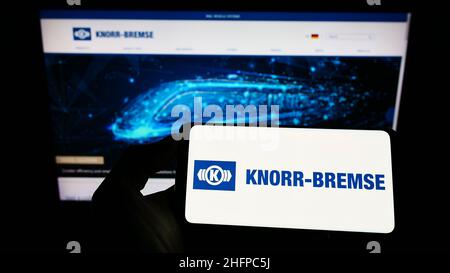 Personne tenant un téléphone portable avec le logo de la société allemande de fabrication Knorr-Bremse AG à l'écran en face de la page web d'affaires.Mise au point sur l'affichage du téléphone. Banque D'Images