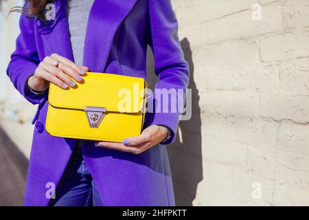 Gros plan de l'élégant sac à main jaune.Jeune femme portant un manteau violet tendance.Vêtements et accessoires pour femmes Spring.Mode Banque D'Images