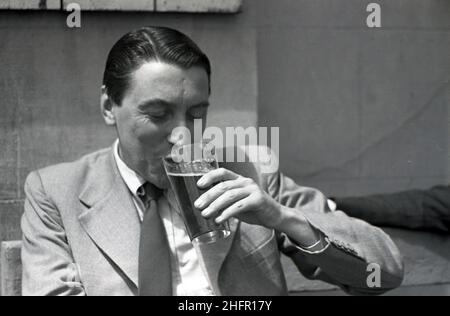 1950s, historique, un anglais bien habillé dans une veste et cravate assis dehors souriant, comme il aime sa pinte de bière, Angleterre, Royaume-Uni. Banque D'Images