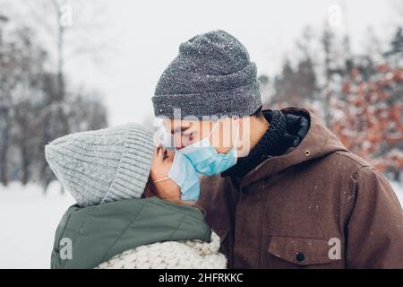 Couple amoureux s'embrassant pour la Saint Valentin dans un parc hivernal enneigé.Couple porter des masques médicaux.Mesures de sécurité en cas de pandémie de covid du coronavirus Banque D'Images