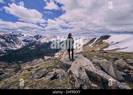 Jeune femme debout sur un rocher exposé dans un champ de neige des montagnes Rocheuses Banque D'Images