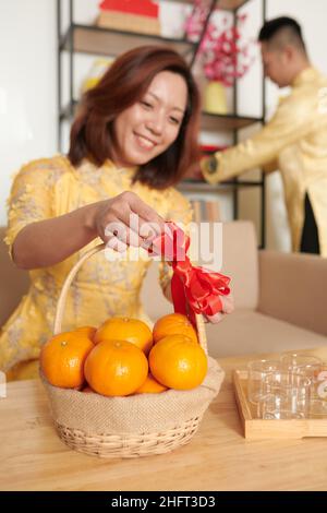 Bonne femme mettant un panier décoré de mandarins sur une table dans le salon pour la célébration de Tet Banque D'Images