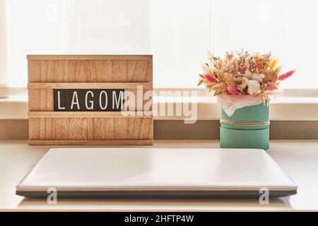 Beau bouquet de fleurs séchées et panneau en bois avec texte LAGOM sur table blanche à côté de l'ordinateur portable Banque D'Images