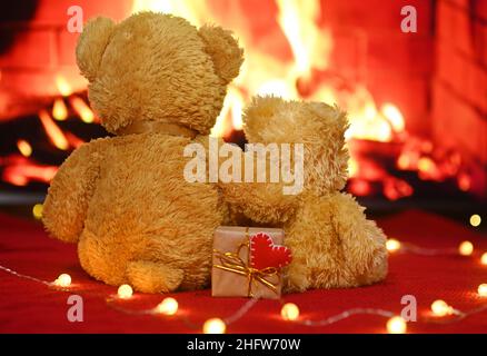 une paire d'ours en peluche s'embrasse contre le fond de la cheminée et tient dans leurs pattes une boîte avec un cadeau et un coeur rouge.Saint-Valentin Banque D'Images