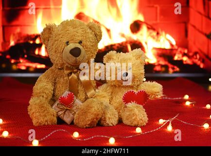 une paire d'ours en peluche est assise sur le fond d'un tissu tricoté rouge et d'une guirlande d'ampoules et tient deux coeurs rouges dans leur Banque D'Images