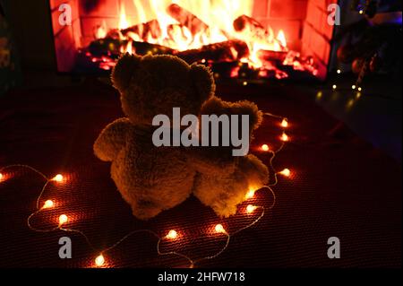 deux adorables ours en peluche s'embrassant l'un l'autre assis sur un tissu écossais rouge tricoté sur le fond d'une guirlande d'ampoules et d'une cheminée. Banque D'Images