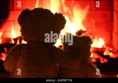 deux ours en peluche s'embrasent et regardent la flamme de la cheminée. Banque D'Images