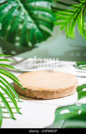 Présentoir publicitaire de produits cosmétiques. Exposition de podium en bois sur fond vert avec des feuilles de palmier et des ombres. Socle vide pour afficher le pack de produits Banque D'Images