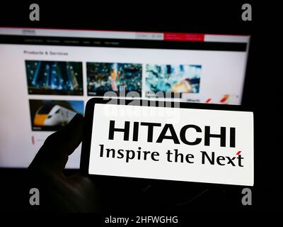 Personne portant un smartphone portant le logo de la société japonaise K.K.Hitachi Seisakusho à l'écran devant le site Web.Mise au point sur l'affichage du téléphone. Banque D'Images