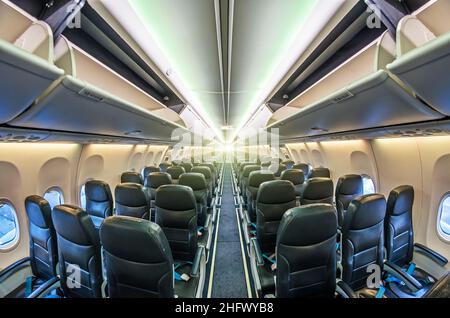 Passage au milieu de l'avion entre les sièges passagers, avec des étagères ouvertes pour les bagages à main Banque D'Images