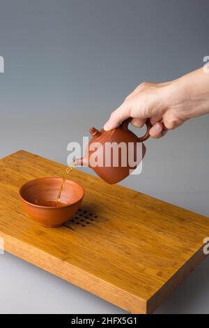 La main d'un homme verse du thé pu erh fraîchement préparé d'une théière en argile dans une tasse traditionnelle.Une tasse sur une table pour les cérémonies du thé. Banque D'Images