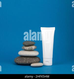 Tube blanc Mockup pour crème sur fond bleu avec une pyramide de pierres naturelles rondes, espace de copie.Concept de soins spa et beauté Banque D'Images