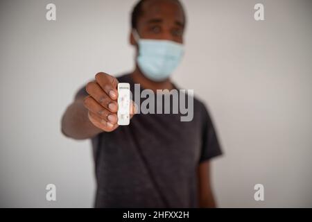 L'homme tient un test Covid-19 en main, il porte un masque chirurgical pendant la pandémie de Cornavirus.Concentrez-vous sur le test Covid-19 Banque D'Images