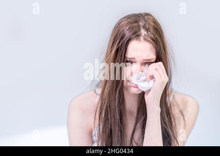 Soyez contrarié.Obtenez la mauvaise nouvelle.Pour souffrir.Cœur brisé.Dépression.Une femme avec un visage sale de mascara s'assoit dans le lit, pleure, essuie ses larmes.Hé Banque D'Images