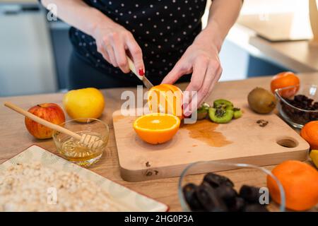 Gros plan sur la main de la femme caucasienne inconnue tenant le couteau coupant kiwi et oranges copier l'espace Banque D'Images