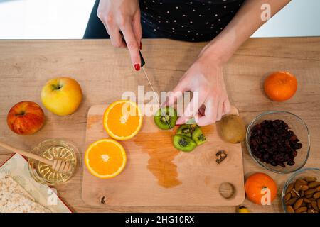 Gros plan sur la main d'une femme caucasienne inconnue tenant un couteau coupant des kiwis et des oranges vue du dessus de l'espace de copie Banque D'Images