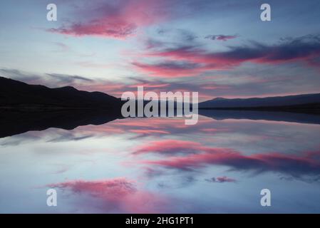 paysage de lac et de montagnes en coucher de soleil rougeâtre avec reflets du ciel Banque D'Images