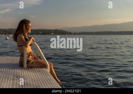 Bonne fille latine assise sur un quai au lac un après-midi chaud Banque D'Images