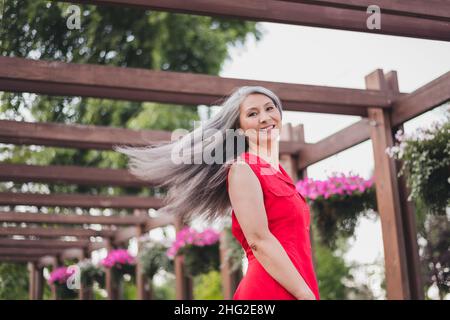 Portrait d'une femme aux cheveux gris joyeuse et attrayante qui s'amuse à jeter des cheveux à l'air frais à l'extérieur Banque D'Images