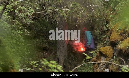 Homme explorer se tenant parmi les arbres verts et tenant feu rouge flamant de l'éclat d'être trouvé par quelqu'un.Perdu dans la nature sauvage et à la recherche de l'aide conc Banque D'Images