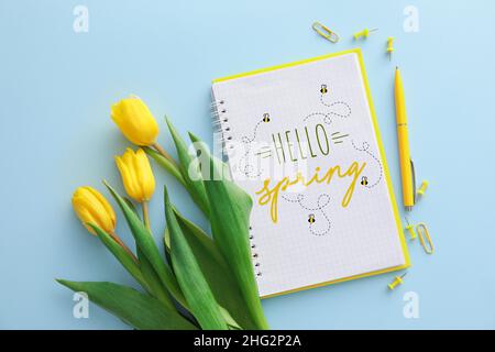 Carnet avec texte HELLO SPRING, fleurs de tulipe jaune et papeterie sur fond bleu Banque D'Images