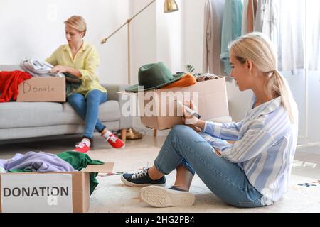 Jeune femme écrivant sur la boîte avec des dons à la maison Banque D'Images