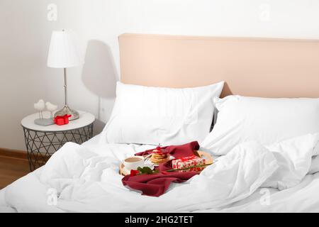 Plateau en bois avec petit déjeuner, rose et cadeau pour la Saint-Valentin sur le lit dans la chambre Banque D'Images