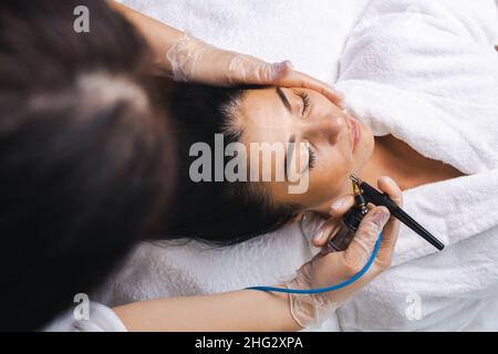 Vue de dessus du visage d'une femme recevant un massage facial électrique de darsonval au salon de beauté.Main du médecin.Visage de beauté.Procédure de beauté de cosmétologie. Banque D'Images