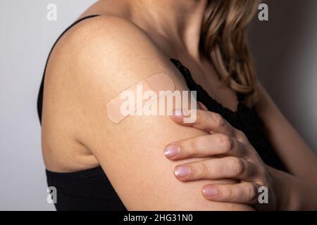 La femme montre l'épaule là où elle a été vaccinée.Patch médical appliqué sur la peau. Banque D'Images