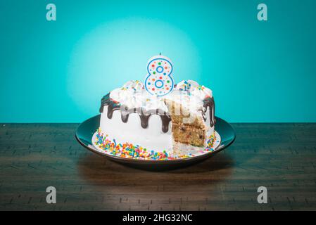 Un gâteau d'anniversaire, manquant une tranche, porte une bougie en forme de numéro 8. Banque D'Images