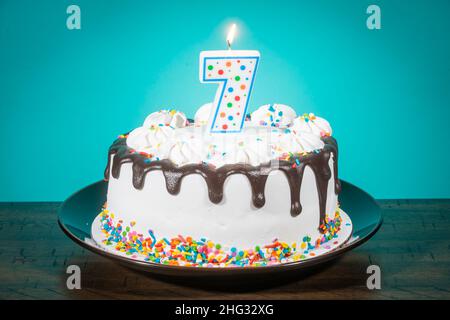 Un gâteau d'anniversaire porte une bougie en forme de numéro 7. Banque D'Images