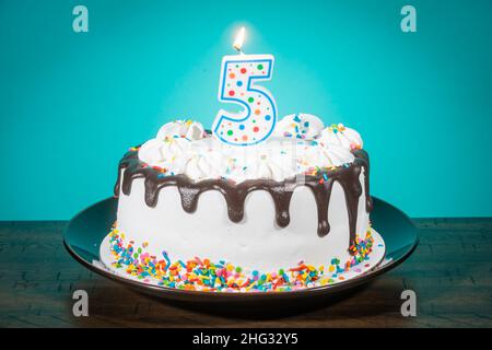 Un gâteau d'anniversaire porte une bougie en forme de numéro 5. Banque D'Images