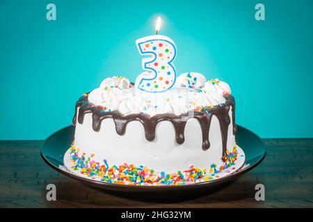 Un gâteau d'anniversaire porte une bougie en forme de numéro 3. Banque D'Images