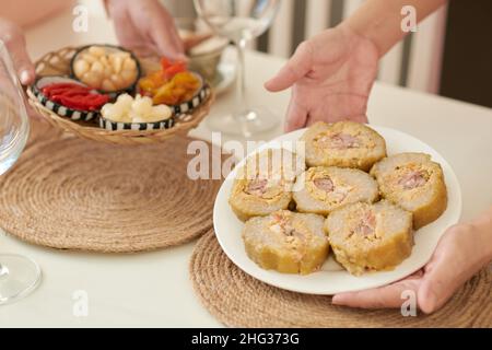 Mains de la femme de ménage en train de mettre une assiette avec un gâteau de riz collant traditionnel vietnamien cylindrique sur la table pour la célébration du nouvel an lunaire Banque D'Images