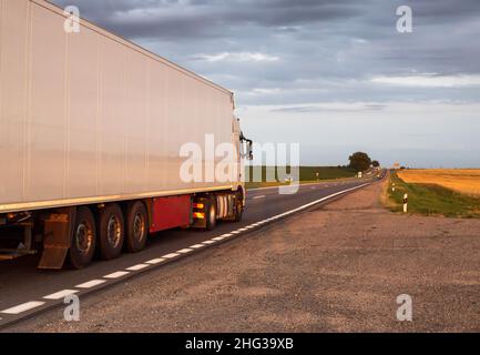 Un camion avec un réfrigérateur blanc semi-remorque transporte des marchandises périssables en été sur fond de champ.Remorques réfrigérées à mai Banque D'Images