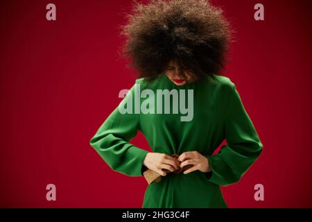 femme avec une coiffure curly luxuriante dans un fond rouge robe verte Banque D'Images
